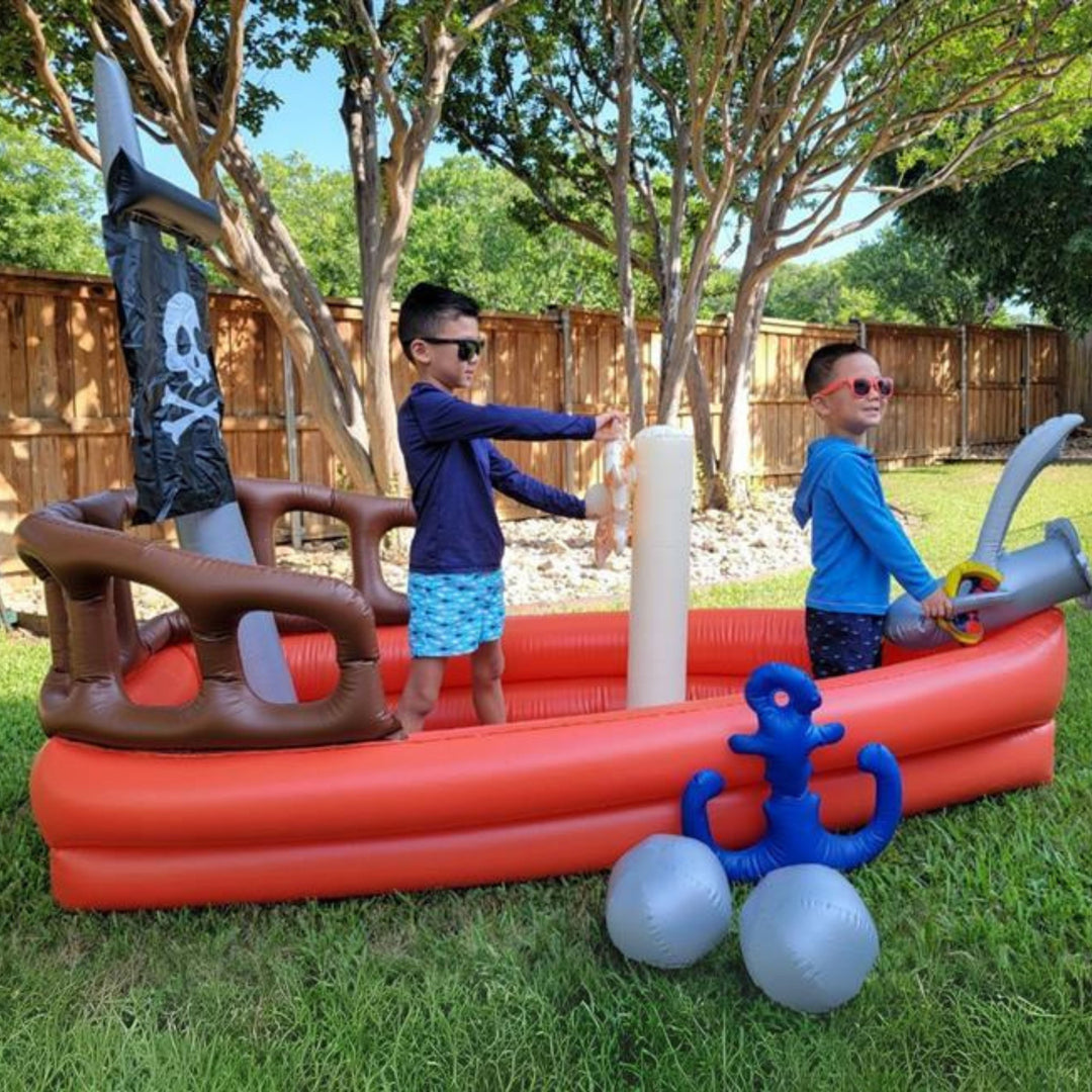 Two boys in a red inflatable pirate ship in a sunny garden