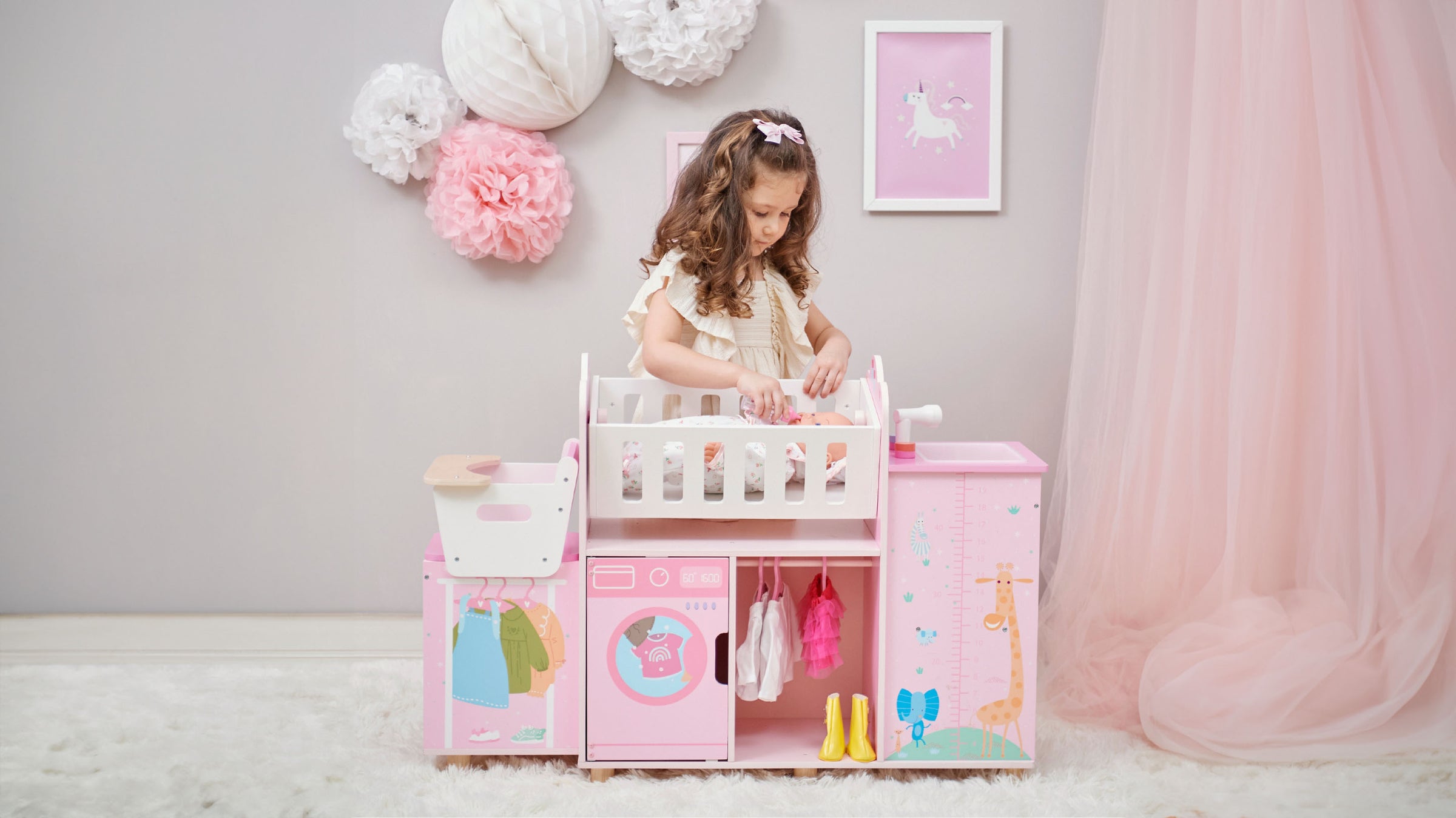 A girl feeding her baby doll laying in the cradle on the baby doll nursery station in pink with animal illustrations.