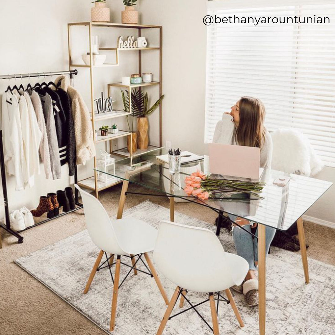 Woman sitting at a glass-topped table working from home with a pair of white chairs across from her.