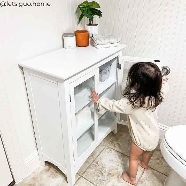 A little girl opening a white floor cabinet in a bathroom