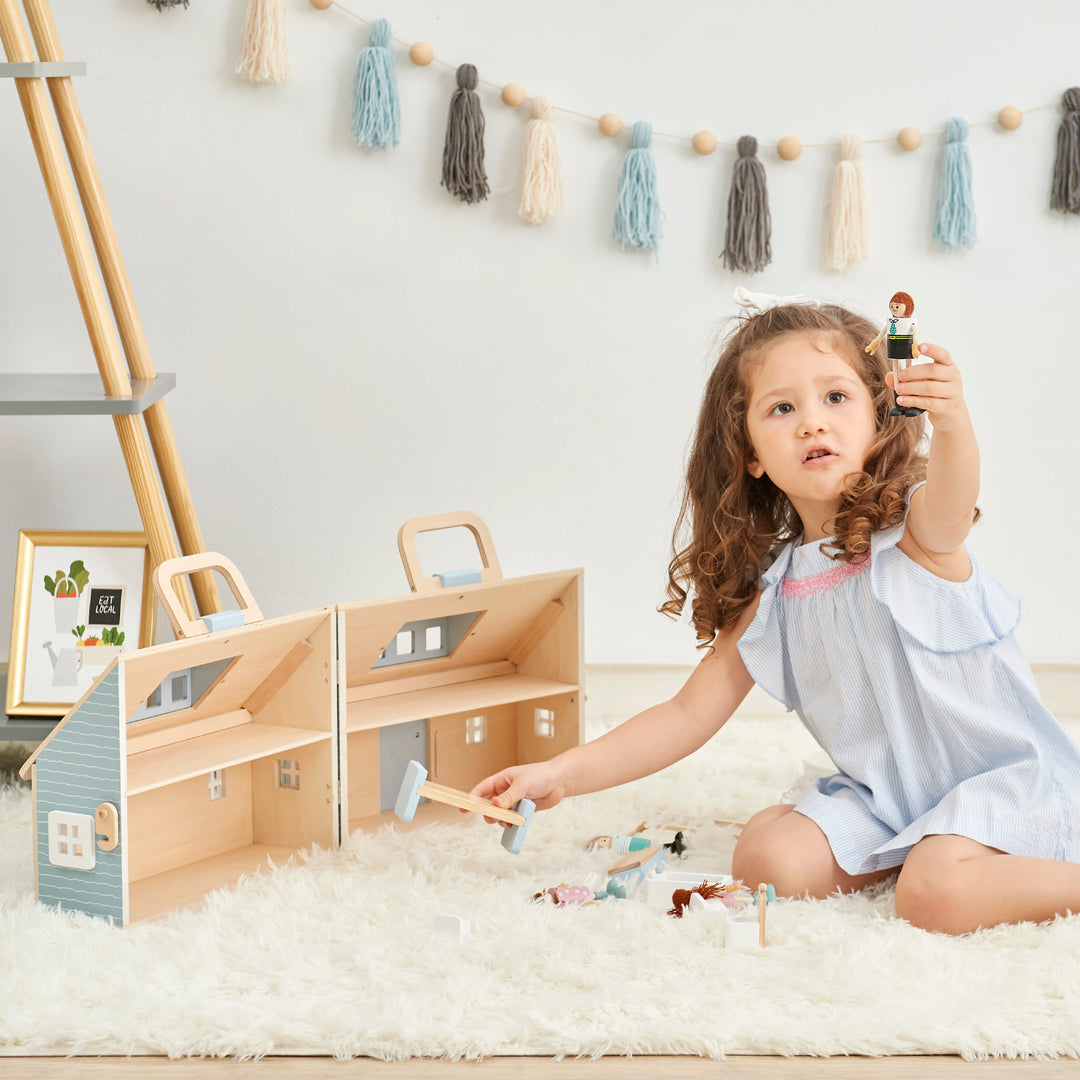 A little girl holding up one of the dolls while placing the bed inside the open cottage.