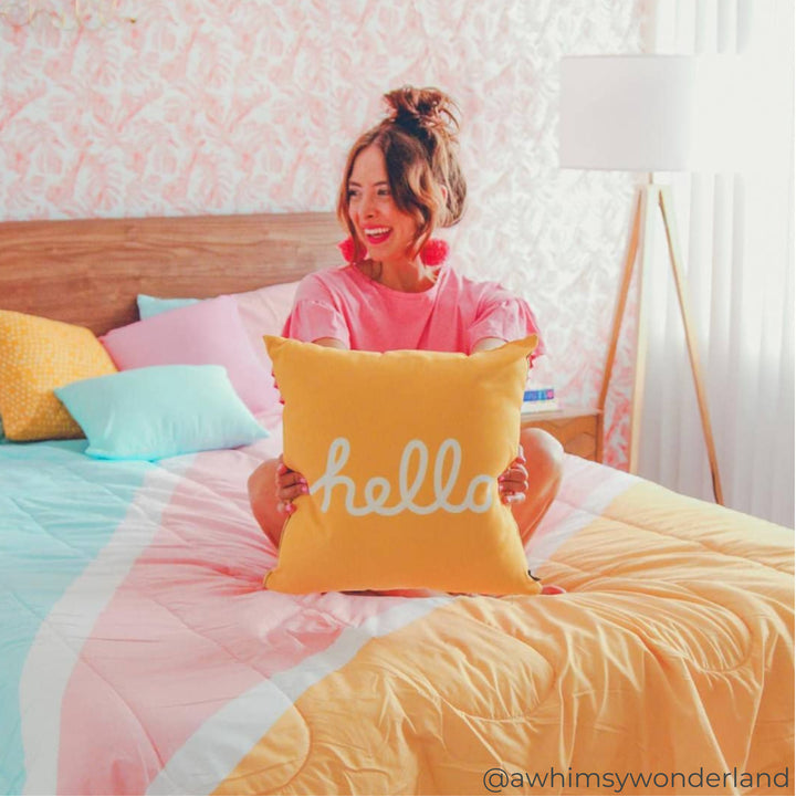 A woman sitting on a colorful bed with a tripod lamp in the corner of the room