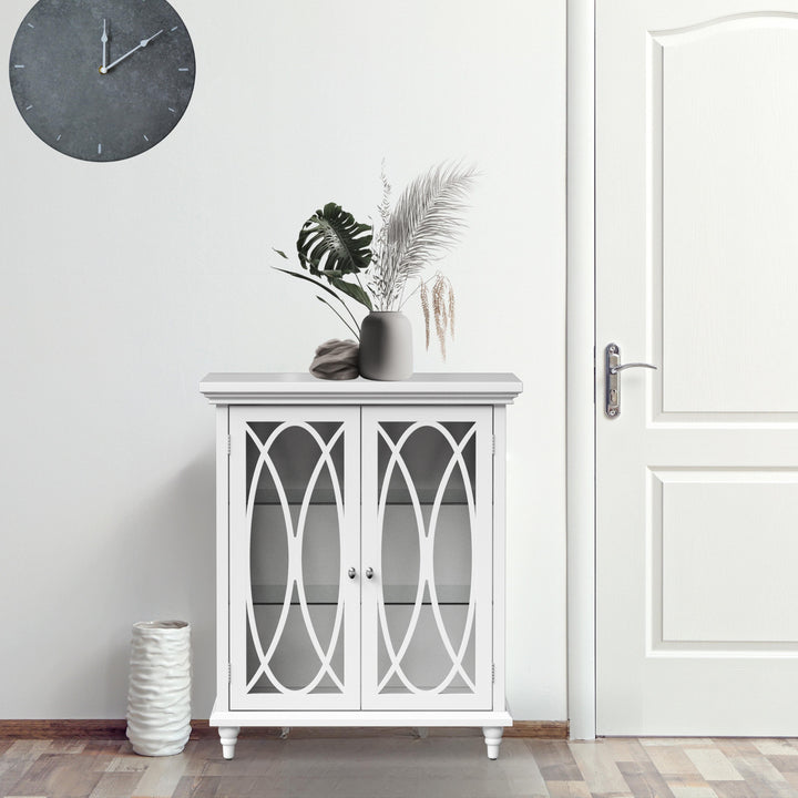 A white floor cabinet with decorative glass doors with decor next to a white door