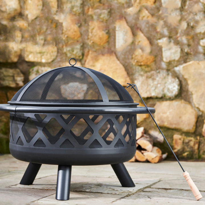 Black mesh firepit in a patio area with fire wood in background