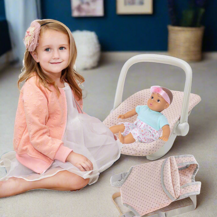 young girl sitting next to her doll in car seat carrier, living room setting