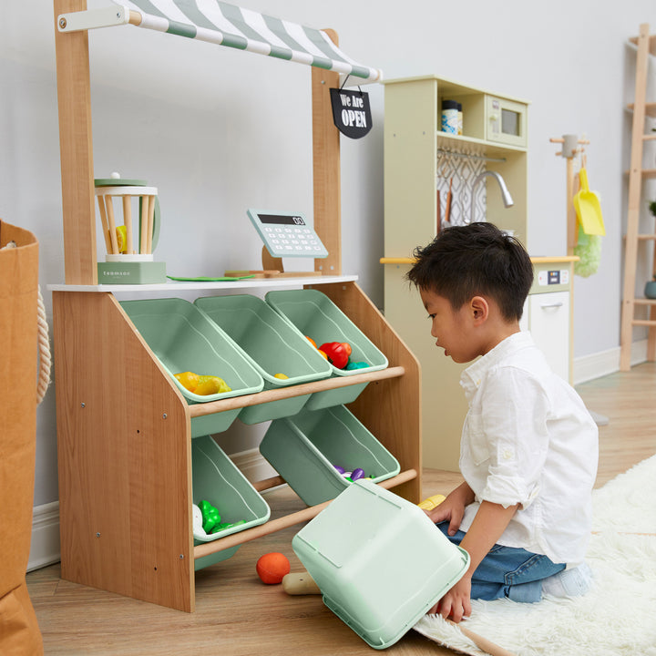 A little boy kneeling in front of  the bins on a play market stand