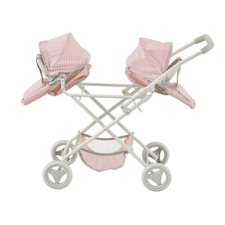 A side view of a double bassinet stroller, pink with gray polka-dotted material and white framework with the bassinets facing opposite directions