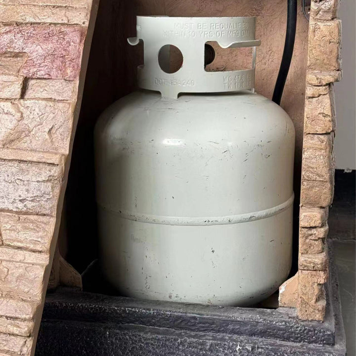 A propane gas tank inside a faux brick propane fire pit