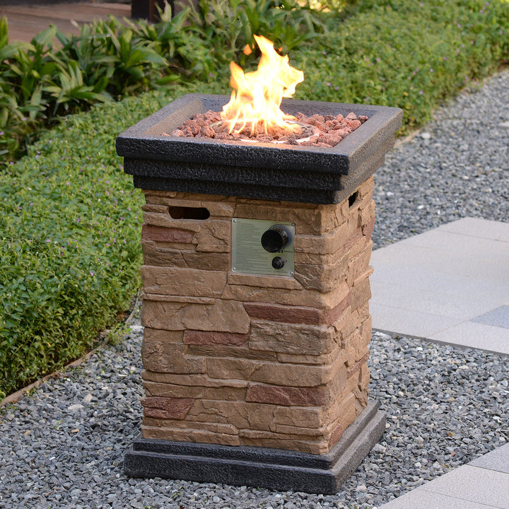 the fire pit column with flames, sitting on gravel in a backyard patio area