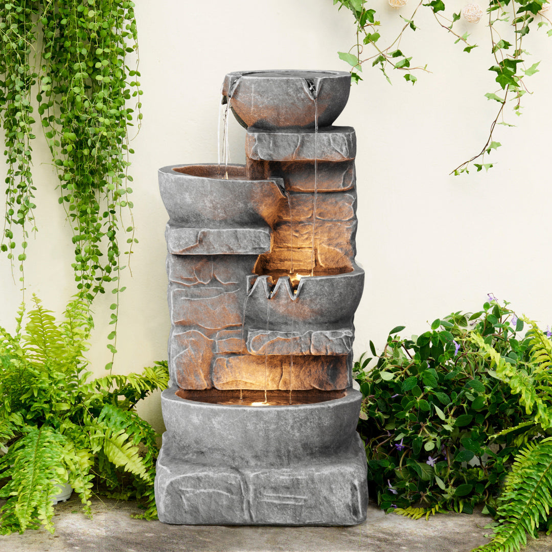 A gray water fountain with staggered bowls on faux stone platform with lights 