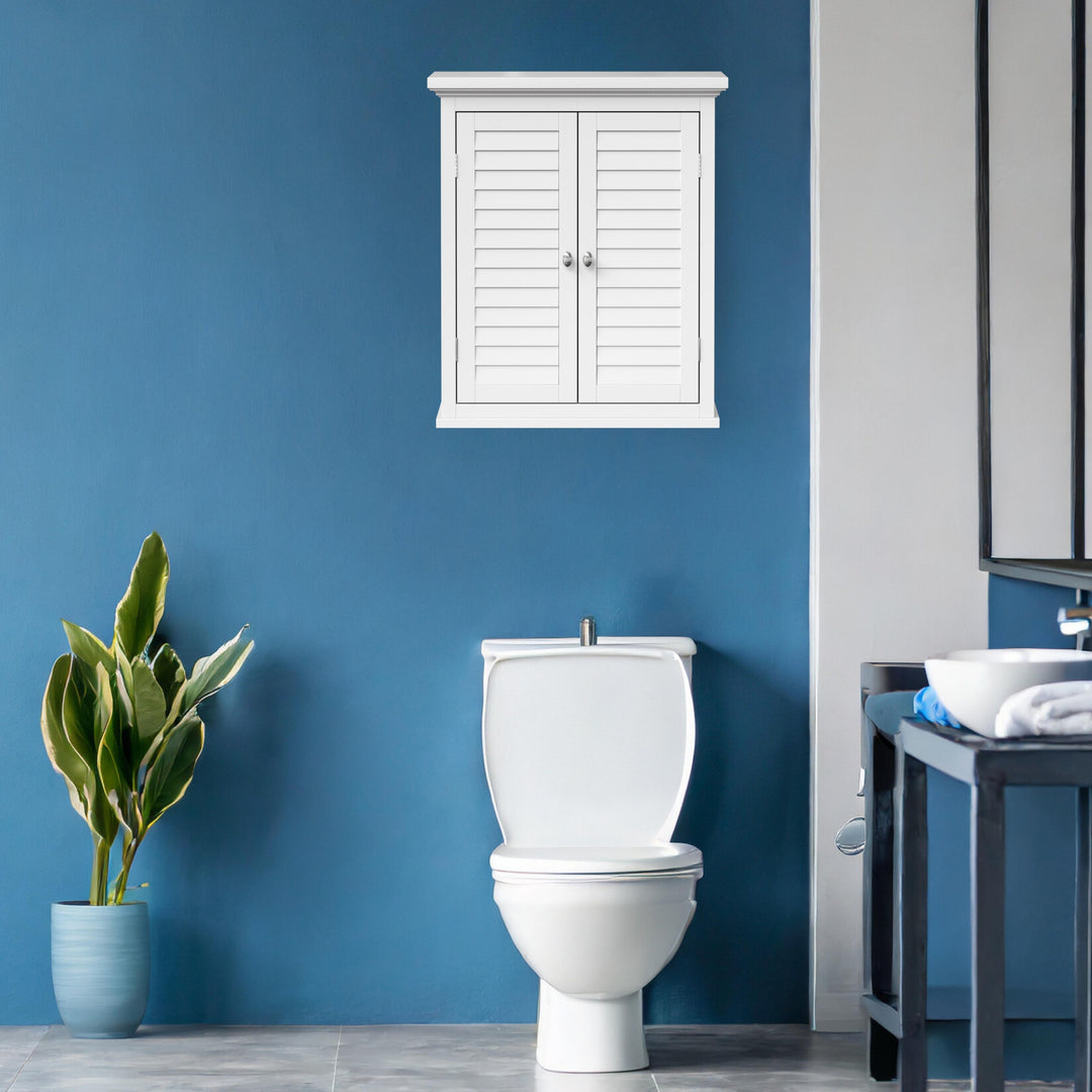 A wall mounted cabinet with faux louvered doors over a toilet in a blue bathroom