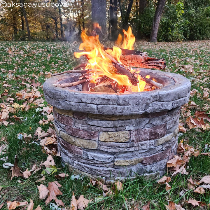 A round faux brick wood burning fire pit with a fire on a fall day