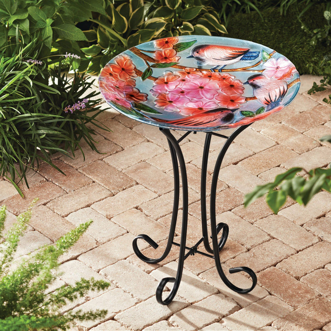 A 17.8" Robins & Blossoms Fusion Glass Birdbath with Metal Stand, Multicolored with a colorful bird on it.