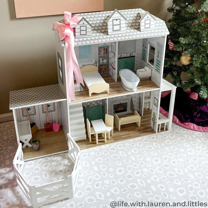 A white dollhouse with furniture next to a Christmas tree