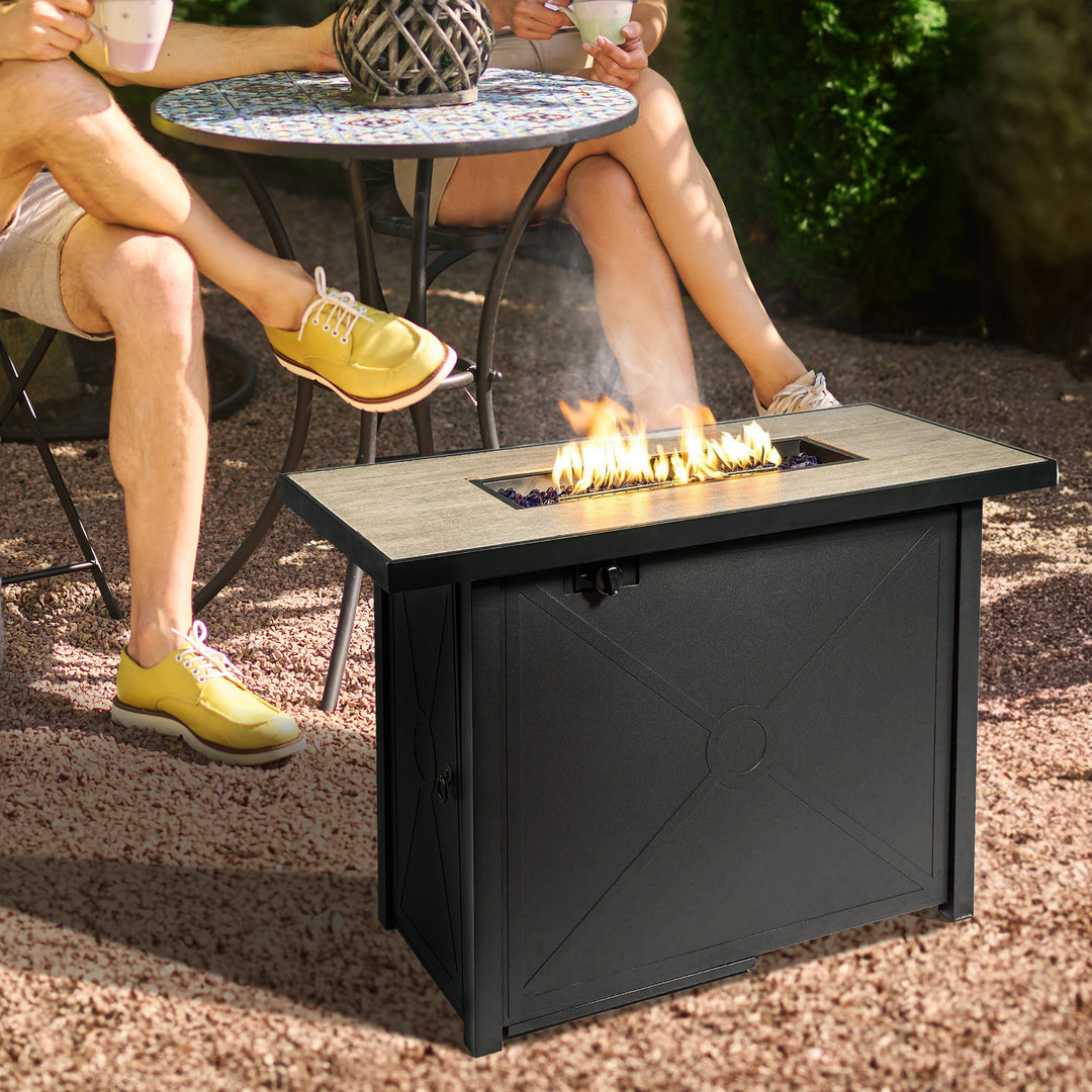 Two adults sitting next to a black propane gas fire pit table with a fire burning