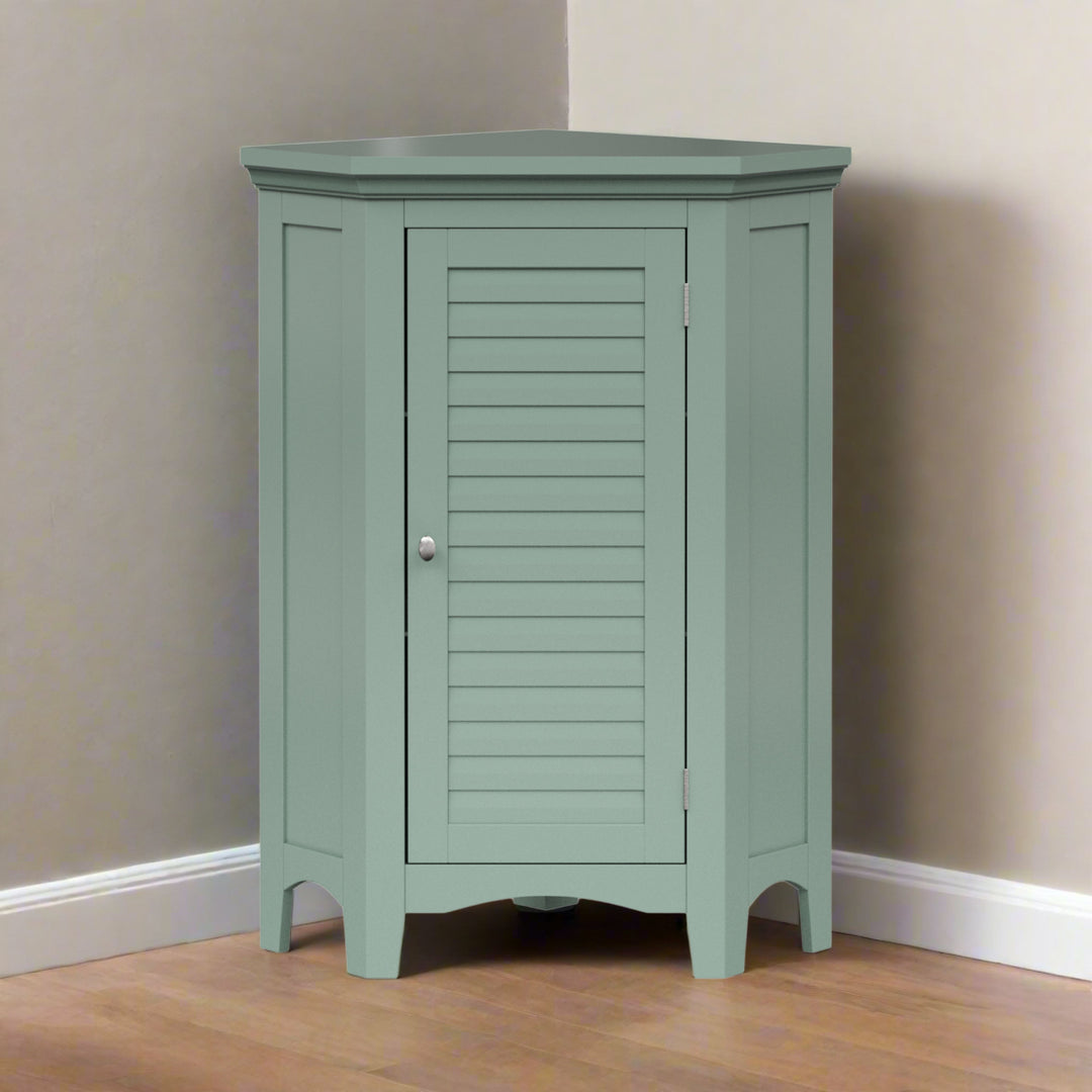 A sage green corner floor cabinet in the corner of a tan room on a hardwood floor.