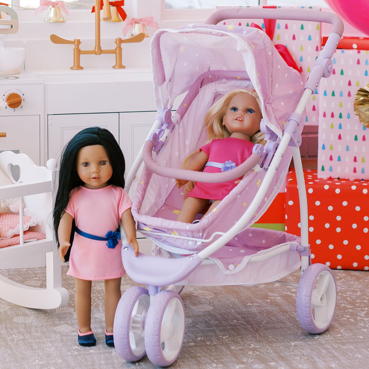 An 18" doll with black hair standing next to a purple stroller with a blonde 18" doll sitting inside