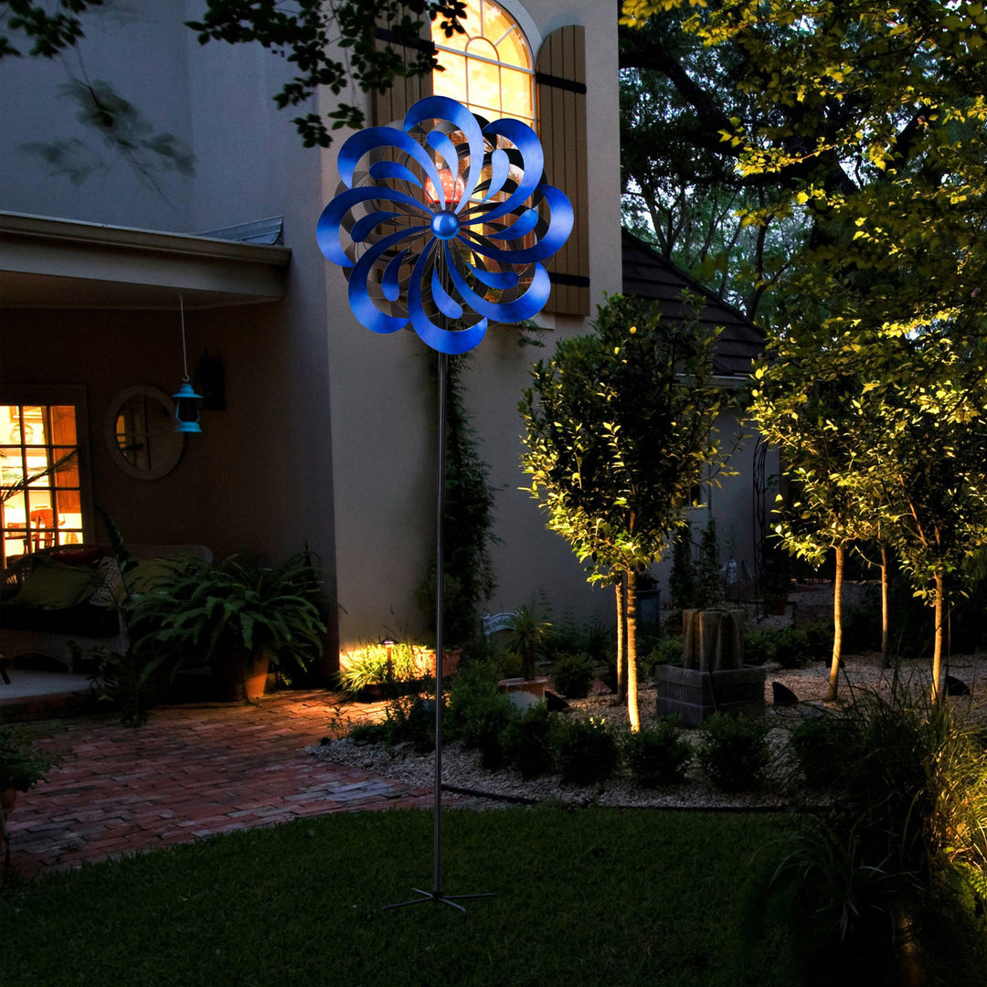 18" dia. x 70" H Solar Metallic Kinetic Windmill Spinner, Blue standing in a twilight-lit yard.