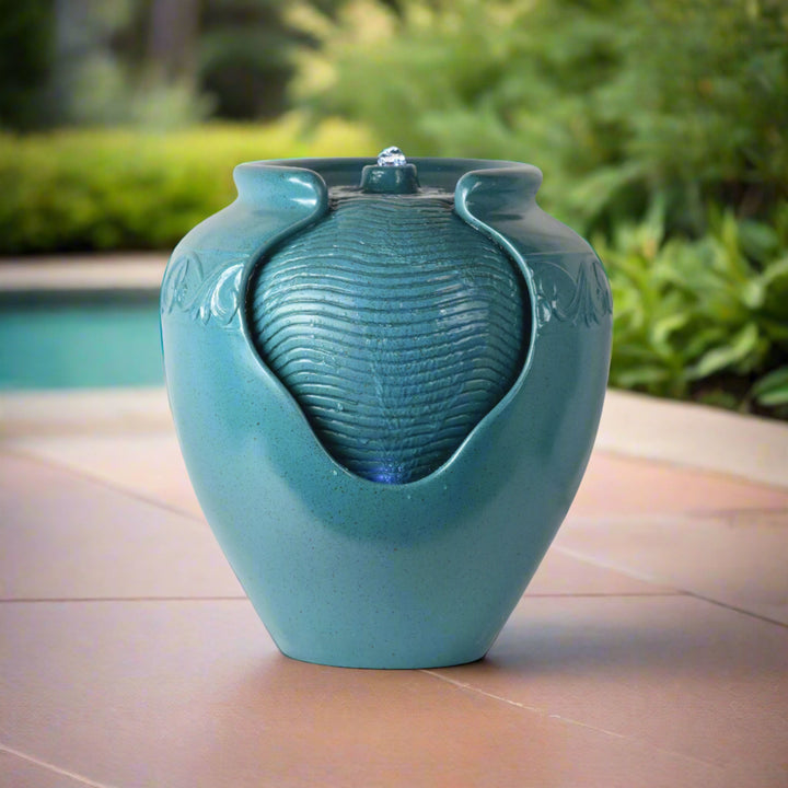 A teal vase shaped water fountain with exposed surface on a patio