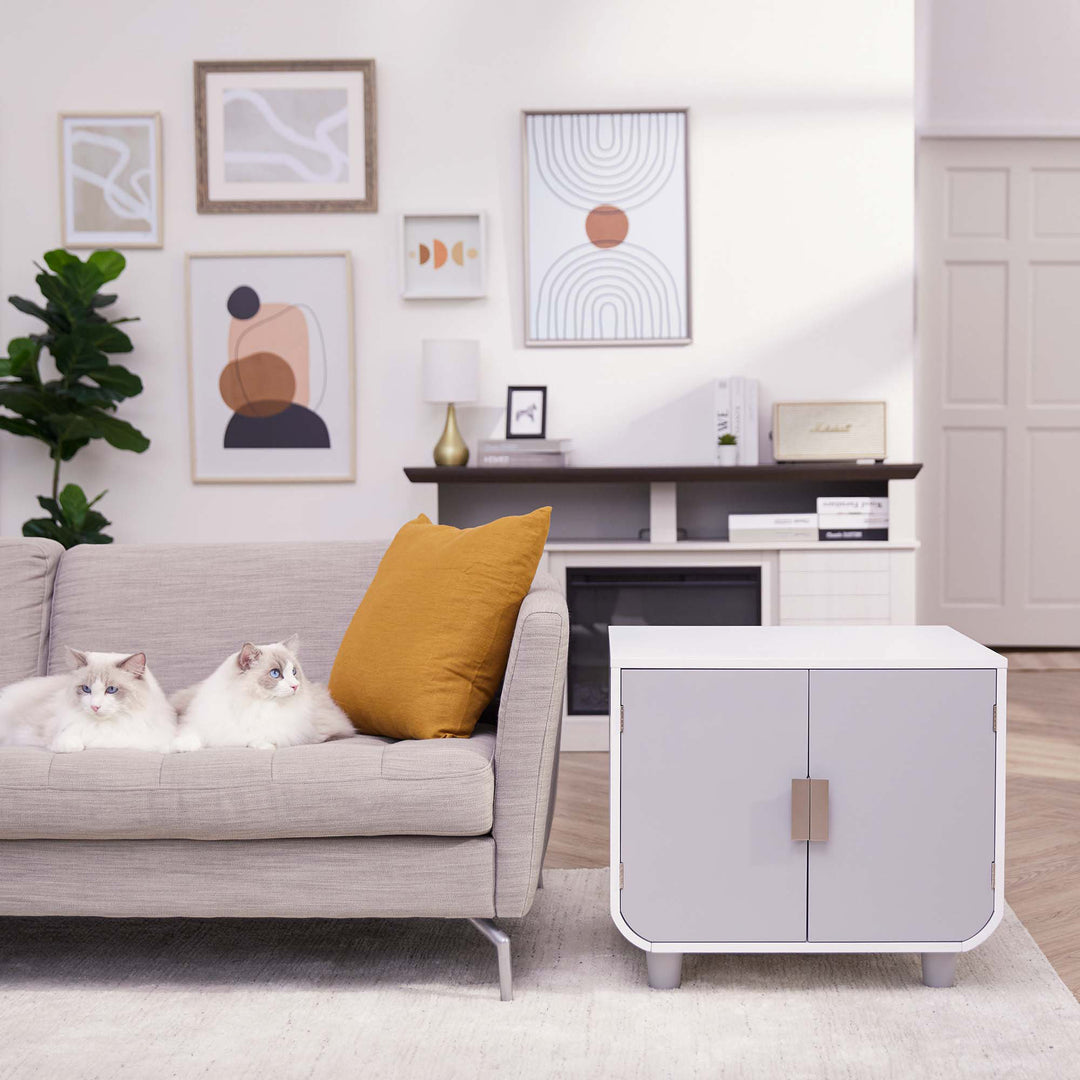 A white and gray cat litter box enclosure next to a sofa with two white cats