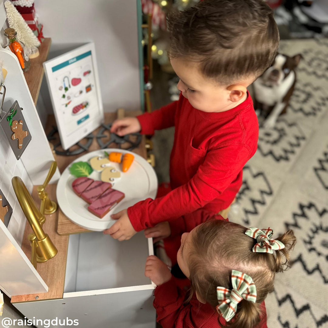 Two kids play with pretend food at a play kitchen