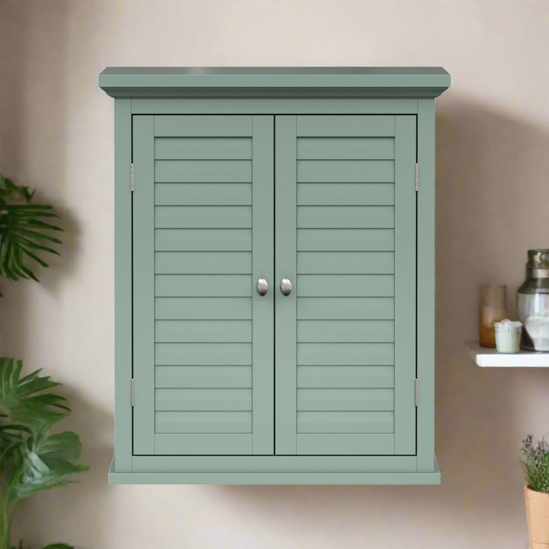 A sage green wall cabinet with brushed silver knobs and two faux louvered doors on a tan wall.