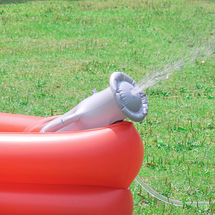 An inflatable red kids pool with an attached gray cannon sprinkler spraying water on a green grass lawn.