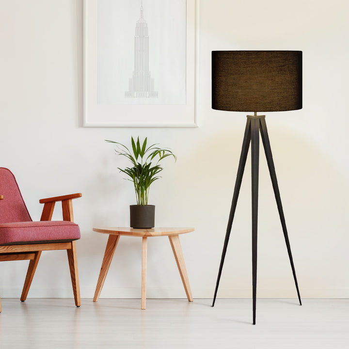 A tripod floor lamp with black shade next to a coral-colored chair