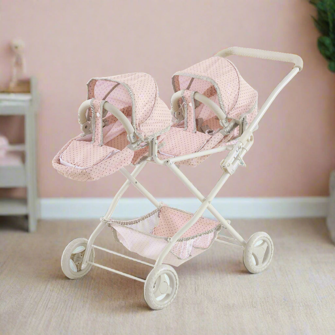 A pink and gray double bassinet stroller sits in a neutral colored play room