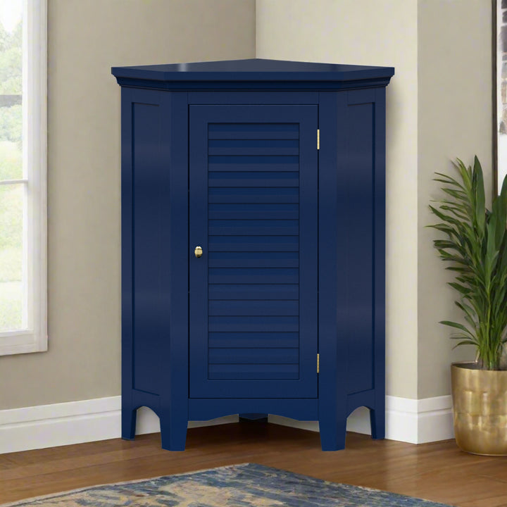 A navy blue corner floor cabinet with gold knobs and two faux louvered doors in the corner of a tan walled room with hard wood floors.