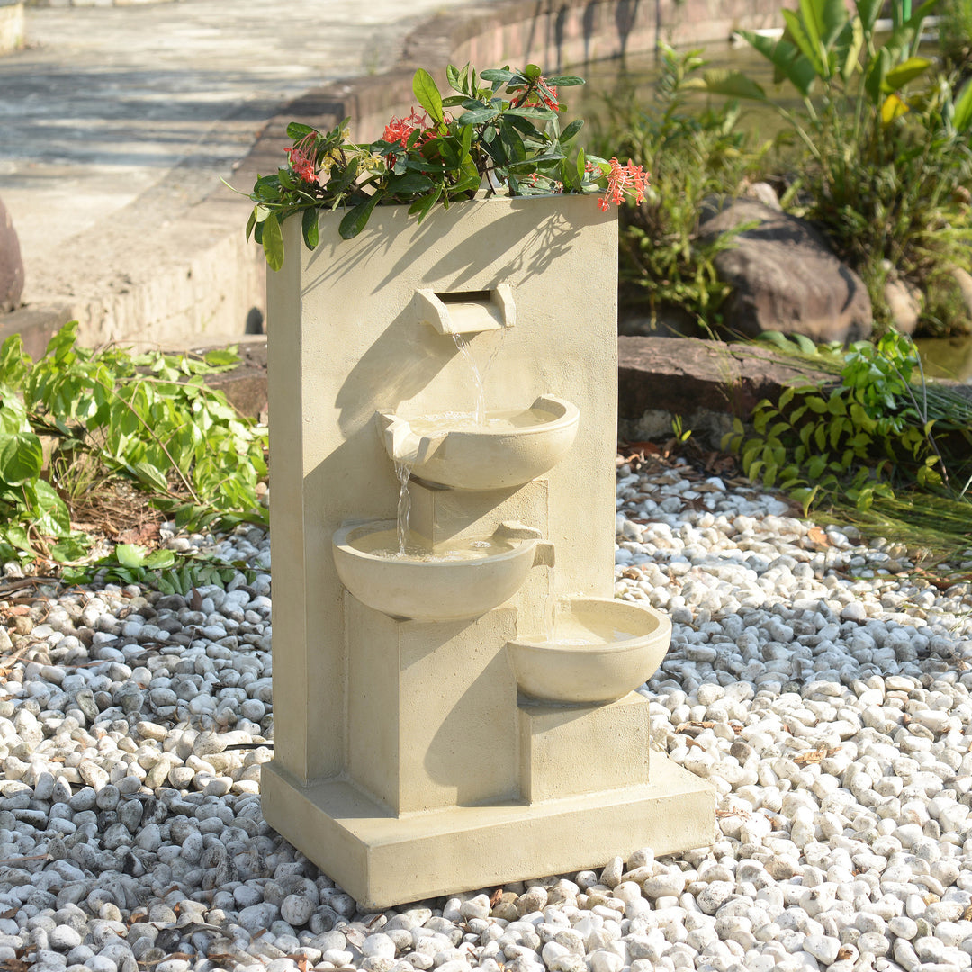 A 29.13" Outdoor Water Fountain with Planter & LED Lights, Natural, set amidst a bed of white pebbles with plants and shrubs all around