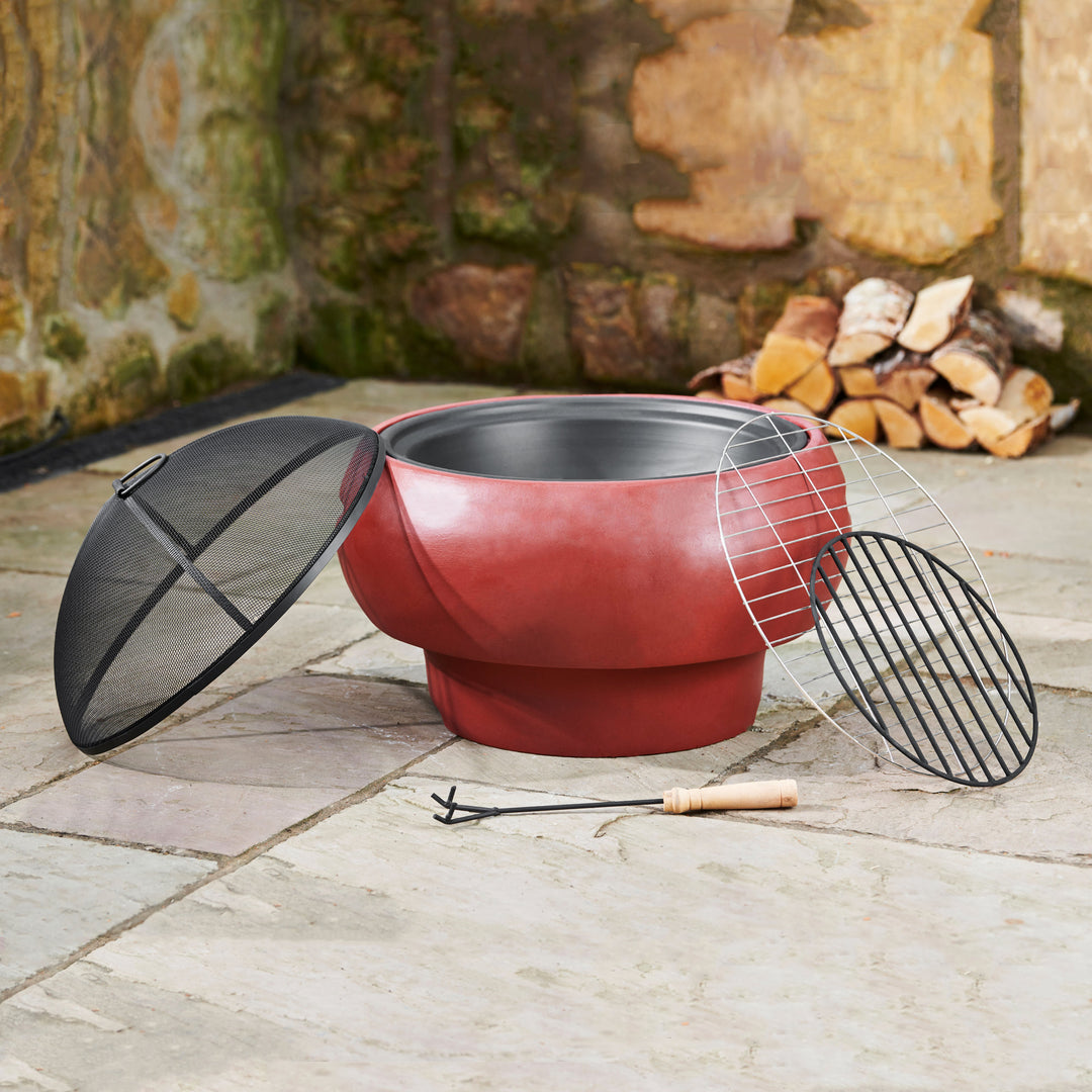 A round red wood burning fire pit with a spark screen, poker and two grates on a slate patio