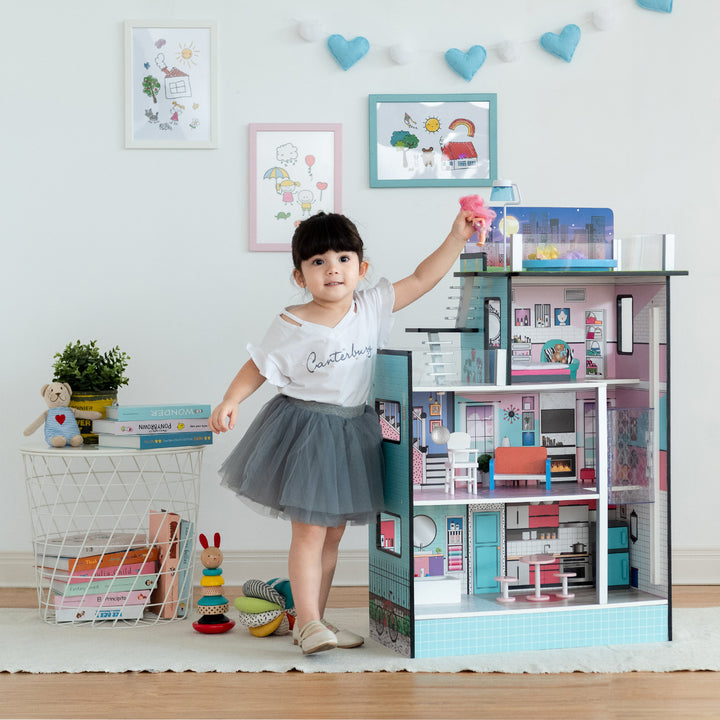 A little girl standing in front of Olivia's Little World Dreamland Barcelona Dollhouse with 10 Accessories, Turquoise/Black reaching to place a doll on the rooftop patio..