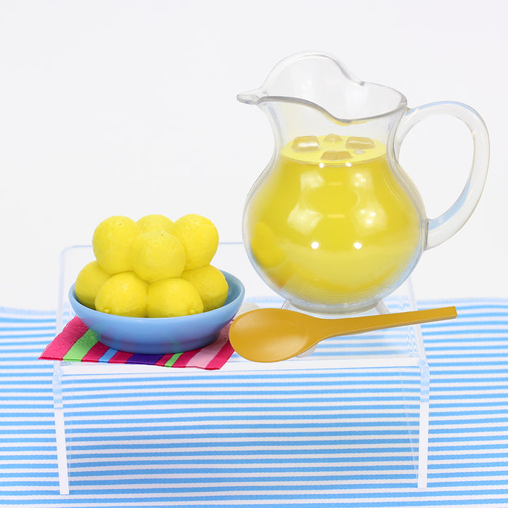 A bowl of Sophia's 21 Piece Desserts and Lemonade Set for 18'' Dolls and a pitcher of liquid on a table.