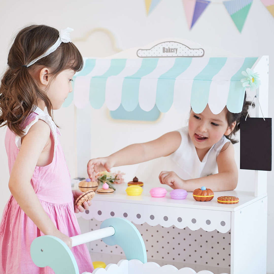 Two children imagine buying and selling baked items at a market stand.