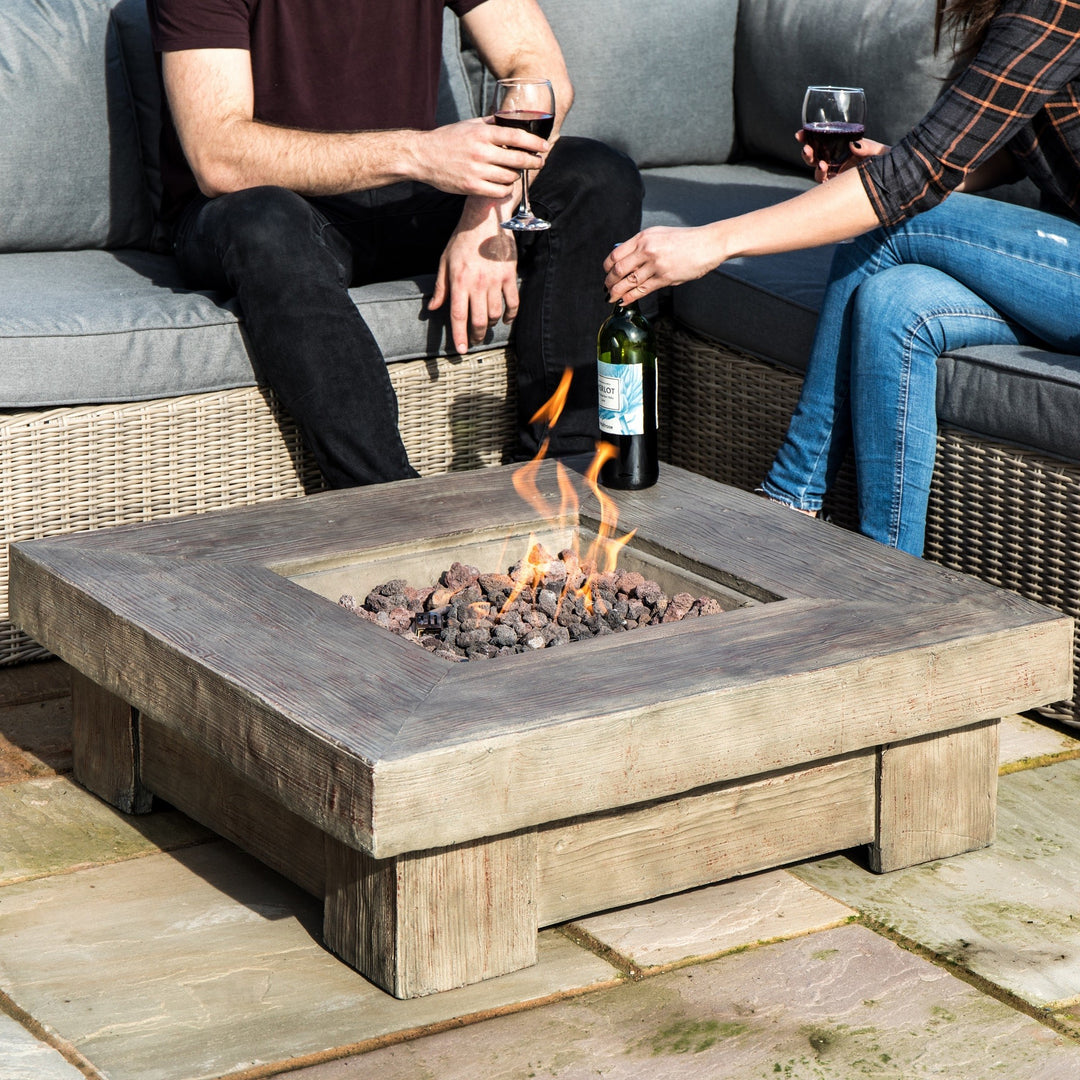 Two people sitting by a Teamson Home 35" Square Retro Wood Look Gas Fire Pit