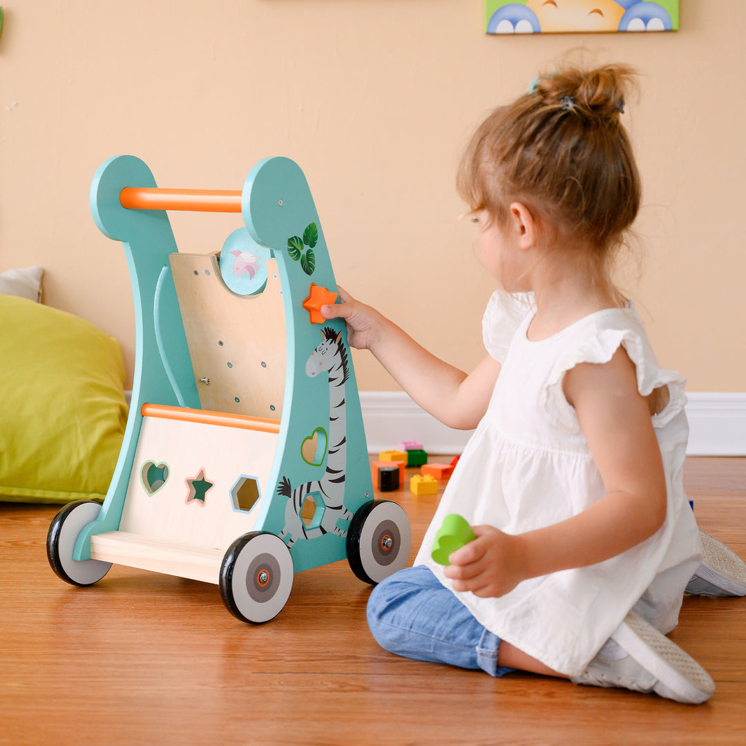 A little girl pushes an orange star into the shape sorter on the side of of the baby walker/activity station.