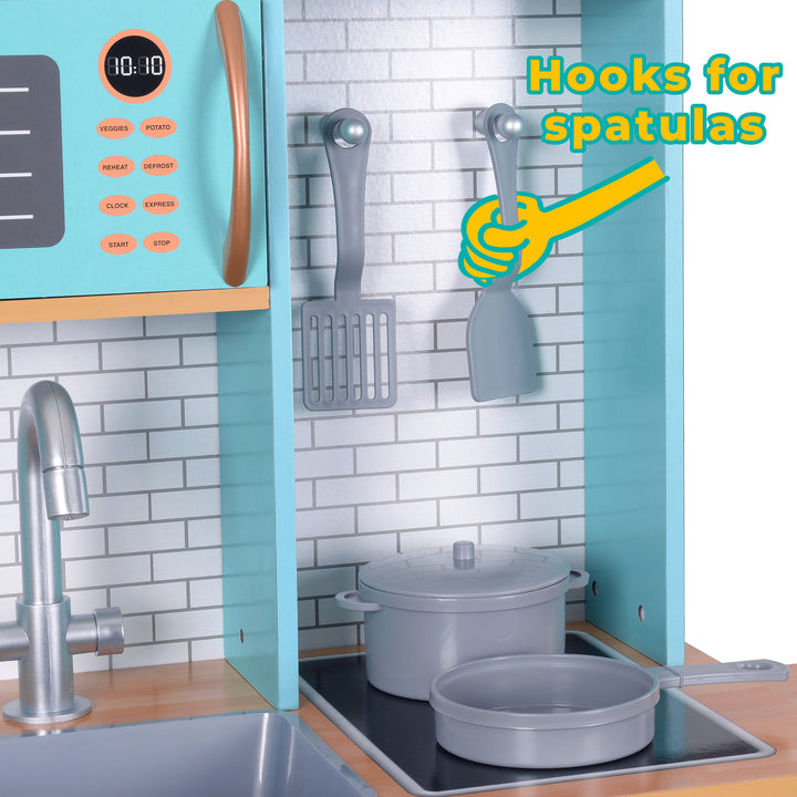 Kitchen wall with hooks holding spatulas, next to a microwave and a sink with a pot on the counter, crafted from Teamson Kids Little Chef Santos Retro Wooden Kitchen Playset, Aqua/White to resemble a kids play kitchen set.