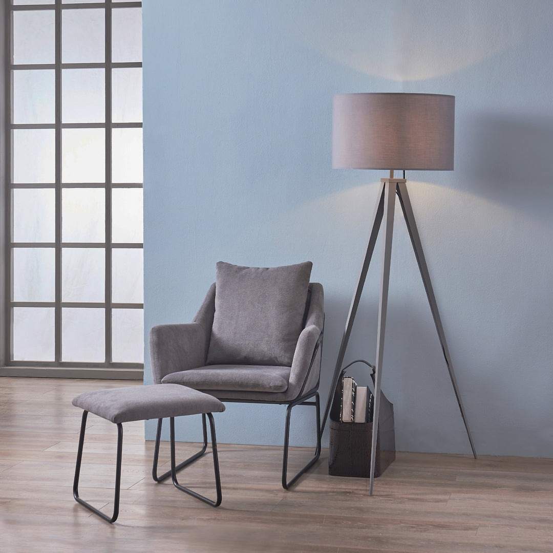 A versatile, modern reading nook with a grey armchair, matching ottoman, Teamson Home Romanza 62" Postmodern Tripod Floor Lamp with Drum Shade in gray, and a small selection of books against a blue wall.