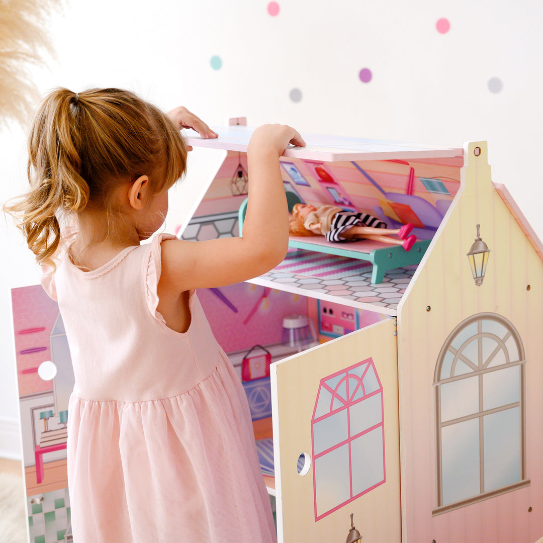 A little girl playing with Olivia's Little World Dreamland Glass-Look Dollhouse and its accessories.