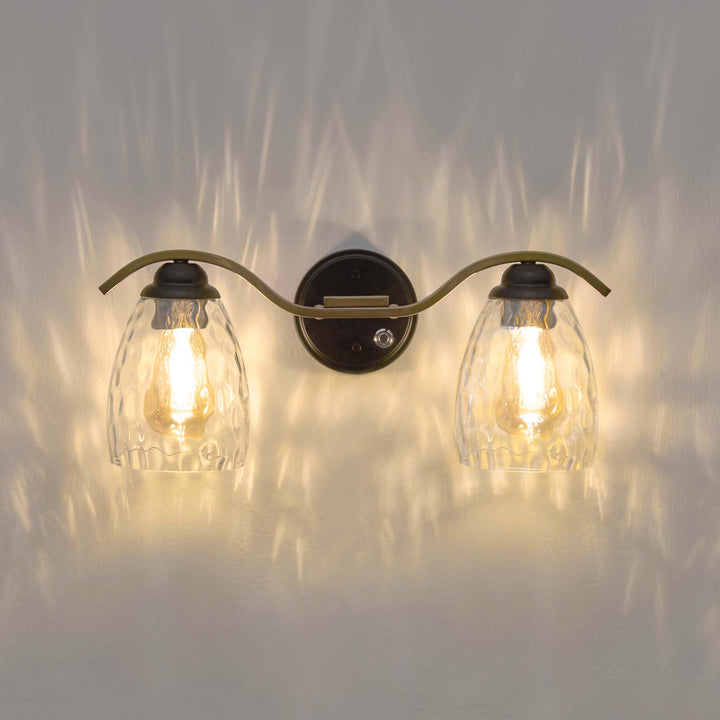 A view of the Teamson Home Heidi 2-Light Vanity Fixture with Clear Hammered Glass Cloche Shades, Black/Brass illuminated and the lighting effect with the glass