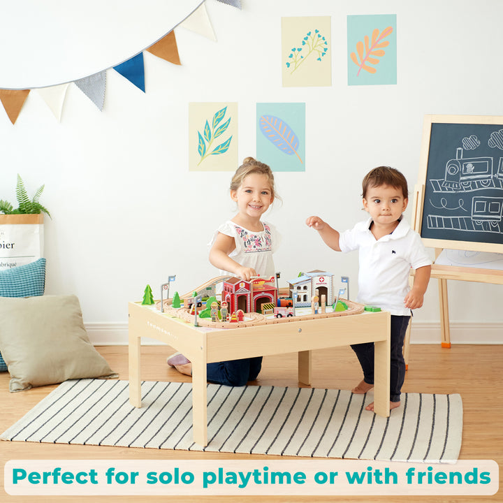 A little girl and a little boy playing with the train set in a playroom.